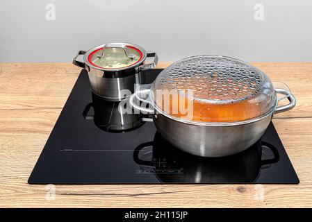 Pots en acier avec un plat de cuisson sur une cuisinière à induction intégrée au plan de travail de la cuisine sur les armoires. Banque D'Images