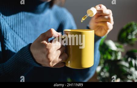 CBD huile de chanvre - femme prenant de l'huile de cannabis dans une tasse de thé pour le traitement de l'anxiété - Focus sur la main gauche Banque D'Images