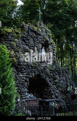 Trzebnica, Pologne - 29 août 2021 : une grotte en pierre avec autel de Sainte Marie, entourée de forêt, devant une église des quatorze Saints Helpers. Banque D'Images