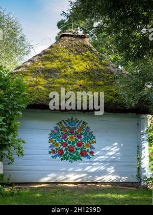 Zalipie, Pologne - 1er août 2021 : chalet traditionnel en bois blanc, avec toit de chaume et murs peints dans un motif floral coloré. Banque D'Images