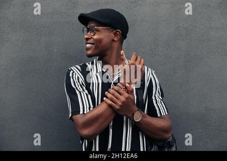 Portrait d'un homme afro-américain contre un mur noir, regardant sur le côté, en souriant largement, portant une chemise et shert, humeur d'été Banque D'Images