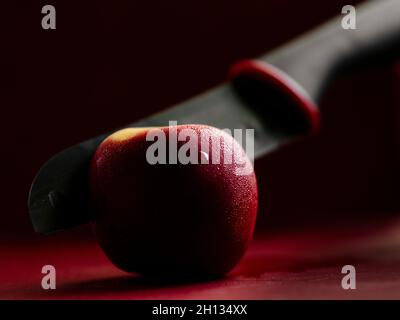 Couteau en céramique noire coupant la pomme rouge sur la planche à découper Banque D'Images