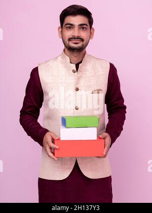 Beau indien en tenue traditionnelle tenant des boîtes-cadeaux à la main dans la pose de bienvenue sur un arrière-plan isolé. Banque D'Images