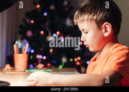 7 yeas vieux garçon assis au bureau et livre de lecture. Arbre de Noël décoré sur fond Banque D'Images