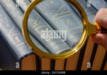 Un homme regarde beaucoup de livres à travers une loupe.Une main avec une loupe.Une collection littéraire de plusieurs volumes numérotés de littérature.Gros plan.Se Banque D'Images