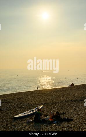 Personnes se détendant sur la plage ou se baignant dans l'eau dans la lumière du soleil d'octobre après-midi, Hove, East Sussex, Angleterre. Banque D'Images