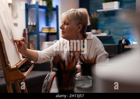 Artiste âgé avec handicap en utilisant un crayon pour dessiner un vase dans un studio d'art.Vieille femme assise en fauteuil roulant tout en travaillant sur un chef-d'œuvre d'art professionnel.Adulte senior handicapé Banque D'Images