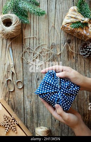 Vacances de Noël sans gaspillage.Mains tenant un cadeau élégant enveloppé dans un tissu en coton sur fond de bois rustique avec des branches en sapin.Style de vie durable sans plastique. Banque D'Images