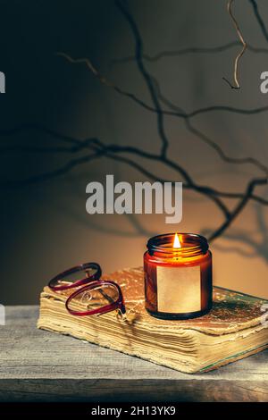 Arrière-plan vintage avec un vieux livre antique, des verres et une bougie dans un pot en verre brûlant la nuit.Les brunchs et les ombres des arbres font des universités sombres et effrayantes Banque D'Images