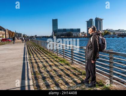 Vue sur la rivière Spree, homme âgé se trouvant à côté de la rivière dans l'ancien quartier de East Harbour à Friedrichshain, Berlin Banque D'Images