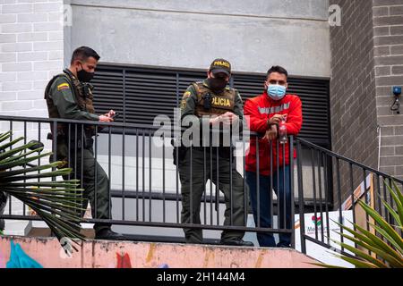 Medellin, Antioquia, Colombie - janvier 6 2021 : Latin Homme vêtu de rouge à côté de deux policiers pentant contre une clôture Banque D'Images