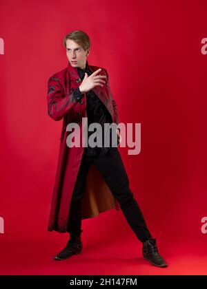 Un jeune homme scandaleux dans un manteau rouge audacieux dans un style noir vintage, photo sur fond rouge Banque D'Images