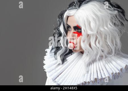 Une drôle de jeune femme scandaleuse dans le maquillage brillant et avec une coiffure noir et blanc souffle une bulle de gomme. Étoile rouge sur l'œil, rock et roll style m Banque D'Images