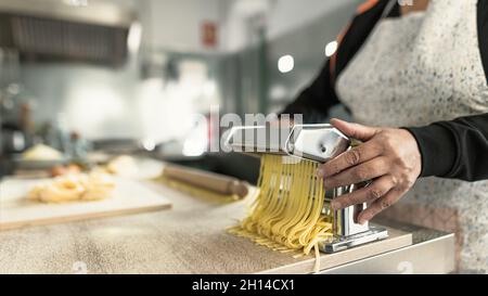 Gros plan des mains de femmes préparant des pâtes fraîches de fettucine à l'aide d'une machine traditionnelle Banque D'Images