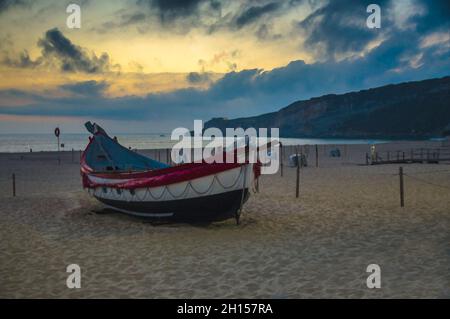 Dessin aquarelle de bateaux en bois colorés sur la plage de Nazaré au crépuscule, bateaux de pêche portugais traditionnels à Nazaré sur la côte, ciel spectaculaire, blanc Banque D'Images