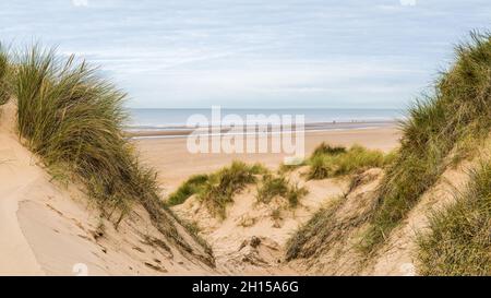 Un panorama à plusieurs images capturé entre deux pics sur les dunes de sable, en regardant vers le bas sur les personnes marchant le long de la plage de Formby près de Liverpool. Banque D'Images