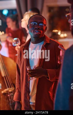 Jeune homme africain tenant un verre avec de l'alcool, il visite la fête Banque D'Images