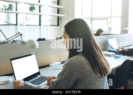 Une fille adulte utilise un ordinateur portable avec un écran blanc vierge pour la maquette Banque D'Images