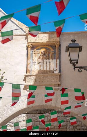 Rue étroite dans la vieille ville de Bari, Puglia, Italie, en une journée d'été avec des drapeaux italiens et l'ancienne image de Saint-Nicolas sculpté dans la pierre, verticale Banque D'Images