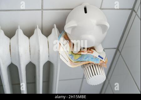 Piggy banque assise sur l'argent sur le thermostat d'un ancien radiateur, concept pour augmenter le coût de la chaleur et de l'énergie en hiver froid, focus choisi, nar Banque D'Images