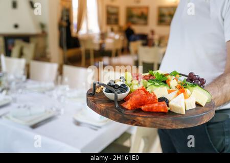 Serveur tenant une planche en bois avec hors-d'œuvre servi dans l'espace de copie du restaurant Banque D'Images