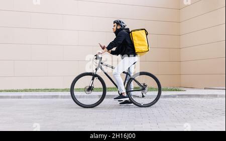 Vue latérale d'un jeune messager avec un homme de sac à dos termal à vélo et à l'aide d'un téléphone mobile dans la ville Banque D'Images