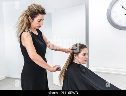 Vue latérale de la jeune femme de maître peignant les cheveux longs dans le salon de coiffure Banque D'Images