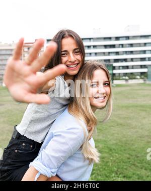 Des amies gaies souriant et regardant l'appareil photo tout en s'amusant sur l'herbe verte dans la cour Banque D'Images