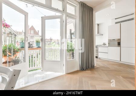 Balcon fenêtres ouvertes dans la cuisine spacieuse avec mobilier blanc et appareils modernes dans l'appartement lumineux Banque D'Images