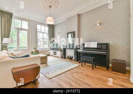 Intérieur de style classique salon avec canapé confortable placé près des fenêtres en face du piano et cheminée dans appartement spacieux et lumineux Banque D'Images