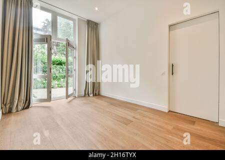 Spacieuse chambre vide avec parquet et portes ouvertes menant au jardin verdoyant avec des plantes luxuriantes dans la maison lumineuse Banque D'Images