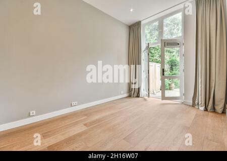 Spacieuse chambre vide avec parquet et portes ouvertes menant au jardin verdoyant avec des plantes luxuriantes dans la maison lumineuse Banque D'Images