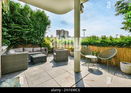 Terrasse spacieuse et vide décorée avec un grand canapé gris confortable avec des coussins près d'une table basse et chaise design avec buche vert vif frais Banque D'Images