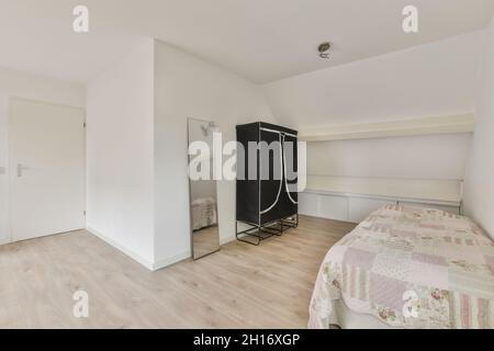 Chambre moderne avec couvercle sur le lit contre le placard et miroir rectangulaire sur le parquet de la maison Banque D'Images
