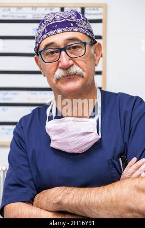 Un vieux médecin sérieux en uniforme médical et un chapeau debout avec les mains pliées et regardant la caméra Banque D'Images