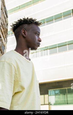 D'en-dessous, un jeune homme afro-américain peu émotionnel portant des vêtements décontractés debout près du mur de pierre Banque D'Images