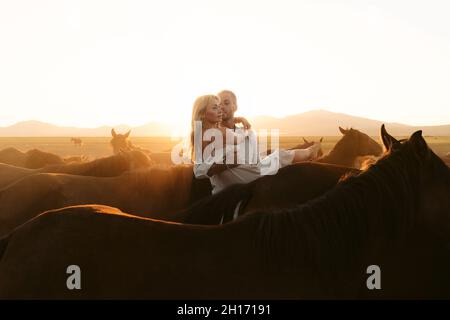 homme tenant une petite amie aux cheveux justes parmi les chevaux dans un pâturage de campagne tout en regardant loin Banque D'Images