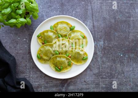 Vue de dessus de savoureux raviolis au basilic décoré avec des pignons de pin servis sur une plaque ronde blanche sur une table dans une cuisine légère Banque D'Images
