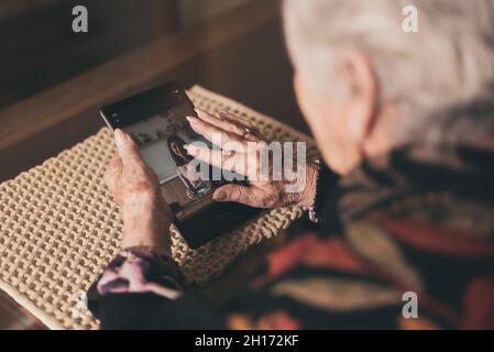 D'une femme âgée, agrandissant et inspectant la photo de la jeune petite-fille sur une tablette tout en étant assise à la table à la maison Banque D'Images