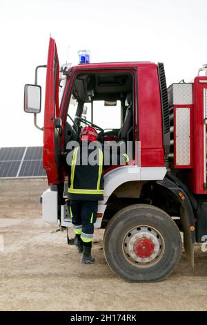 De derrière toute la longueur d'un pompier méconnaissable portant un uniforme de protection grimpant sur un camion de pompiers avec sirène sur le dessus en journée Banque D'Images