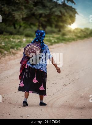 Ancienne femme de brousse du Kalahari central, village de New Xade au Botswana, marchant sur une route de terre Banque D'Images
