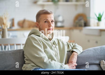 Belle femme mûre dans des vêtements décontractés rêvant de quelque chose tout en se relaxant sur le canapé à la maison Banque D'Images