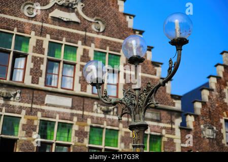 Gand, Belgique - octobre 9.2021: Gros plan de trois vieilles lampes de rue armées avec façade de maison de pignon étagée belge typique sur fond bleu ciel Banque D'Images