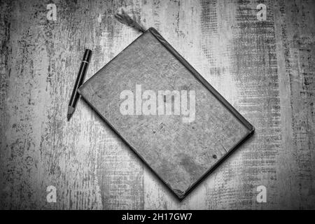 plan d'examen noir et blanc photo d'un ancien carnet d'esquisses fermé très utilisé et crayon sur une surface en bois robuste usée Banque D'Images
