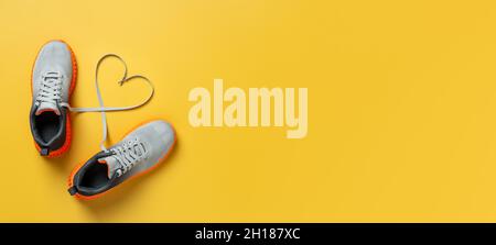 Lacets en forme de coeur entre les sneakers en mesh gris sur fond jaune vif.Chaussures de sport en textile stylées.Maquette de bannière large vierge Banque D'Images