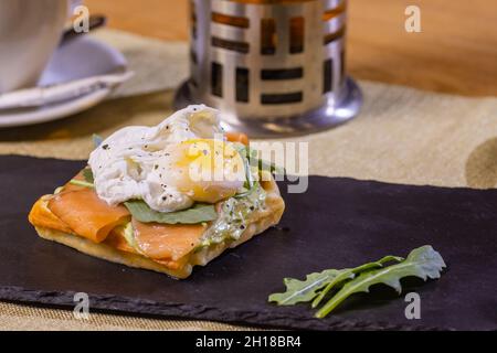 Pain grillé aux œufs pochés, saumon fumé, avocat, tomate grillée et jeunes épinards Banque D'Images