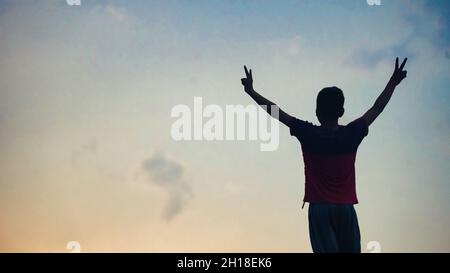 silhouette de garçon debout sur un toit au coucher du soleil.Jeune adulte levant les bras sur le toit au coucher du soleil Banque D'Images