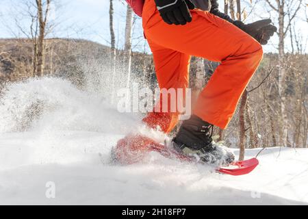 Raquettes marchant dans la neige.Gros plan sur les jambes d'un homme athlète courant en raquettes blanches à neige en poudre, portant une chaussure de ski Banque D'Images