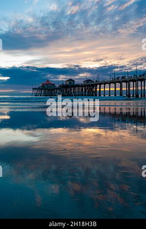 La jetée de Huntington Beach et réflexions sur la plage humide au coucher du soleil.Huntington Beach, Californie. Banque D'Images