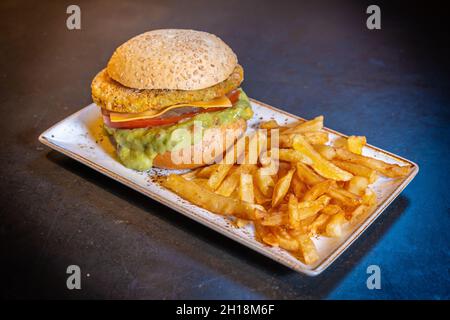 Gros plan d'un hamburger végétalien avec guacamole et frites sur une assiette blanche sur fond noir Banque D'Images